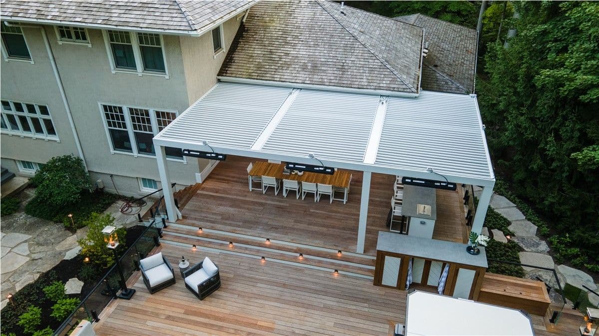 An aerial view of a large brown wood deck with a white Struxure pergola spanning the width.