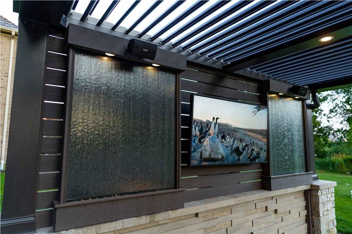A TV mounted on a privacy wall with water features on either side.