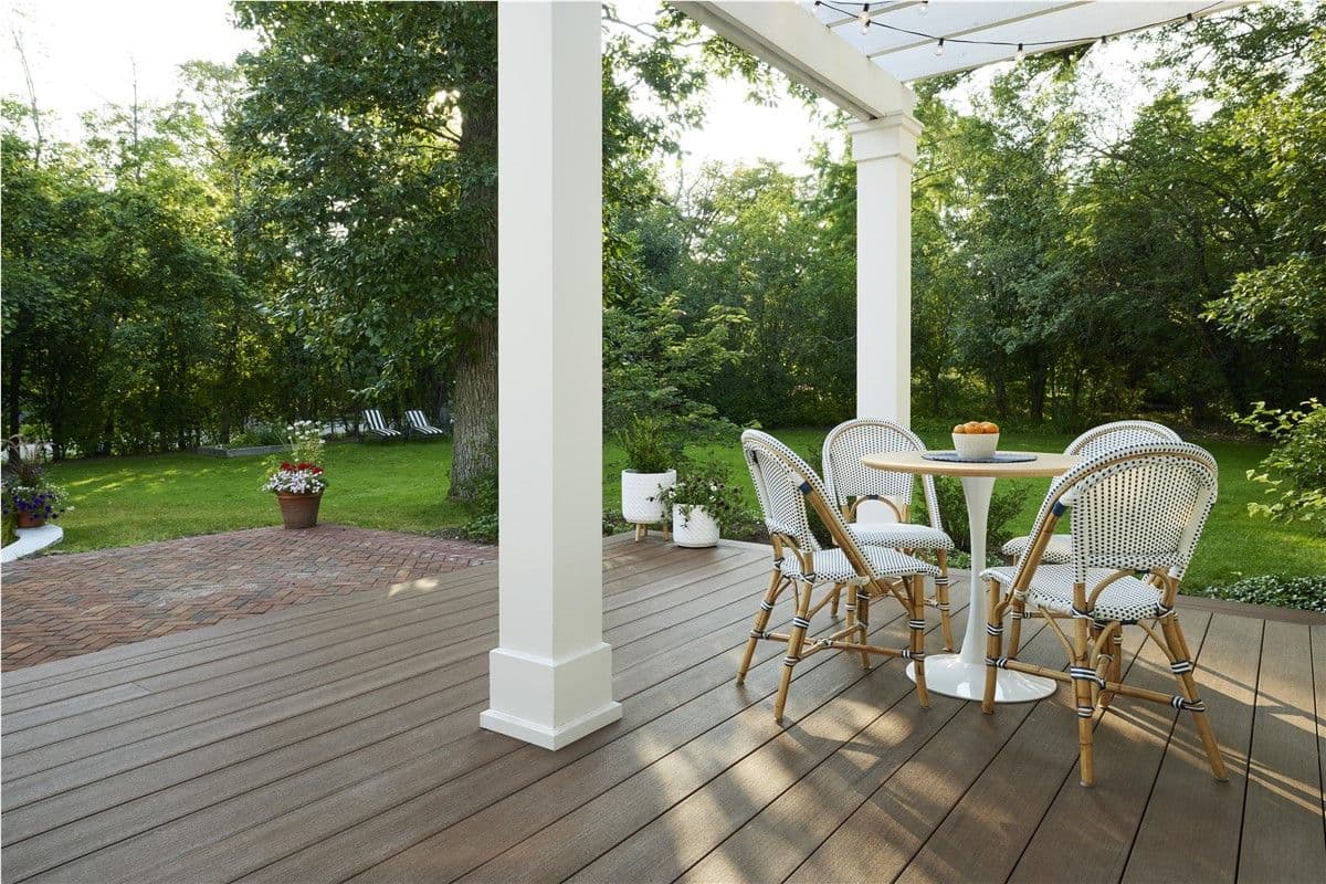 White wicker patio chairs sit around a small table on a deck overlooking a yard and patio.