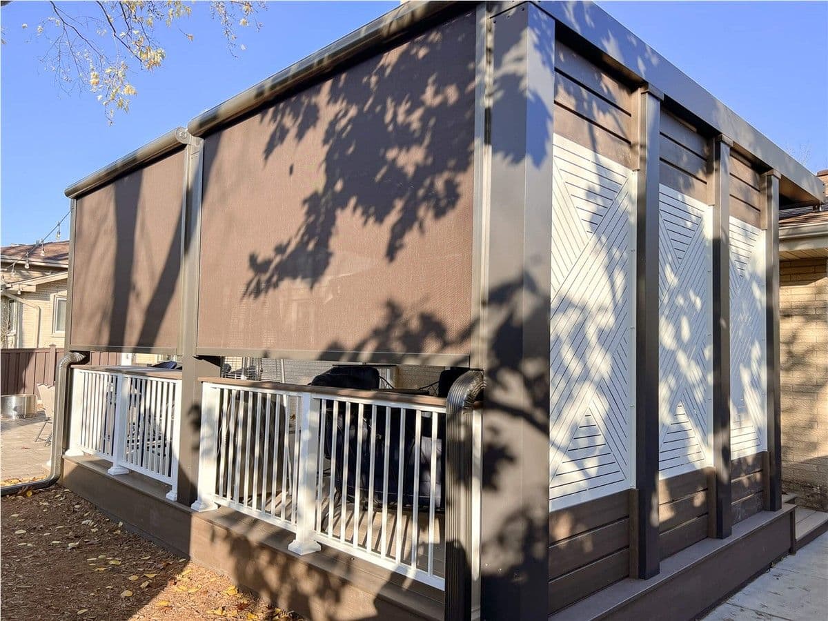A brown and white deck with Struxure pergola. Motorized sun shades hang from the front on the left and a white and brown geometric privacy wall is on the right.