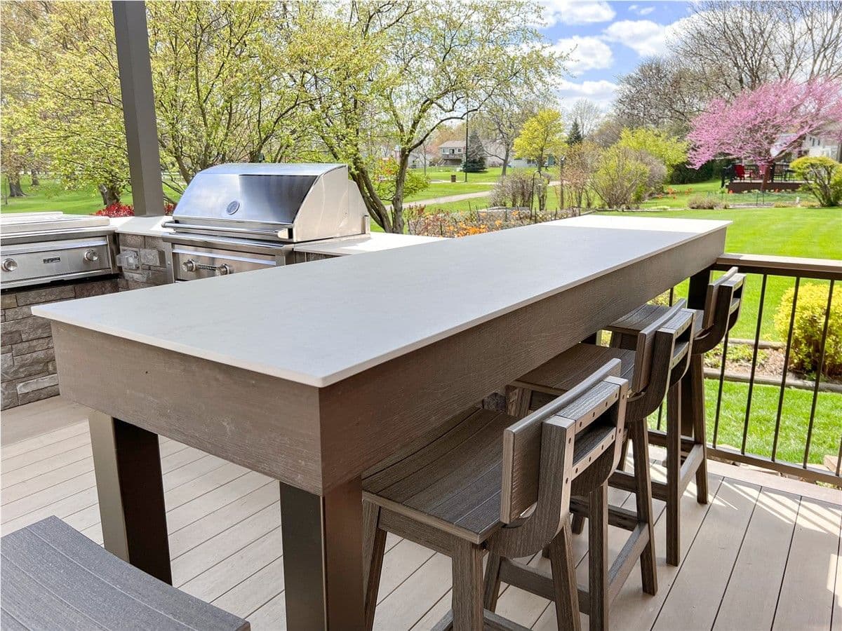 Dark brown high-top bar seating with a light countertop and bar stools on a deck. A grill is visible in the background.