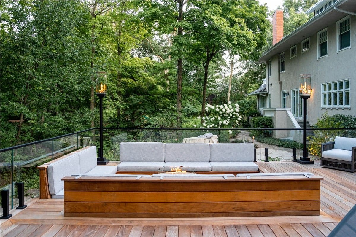 A deck with sunken bench seating around a firepit looks out to a yard full of trees.