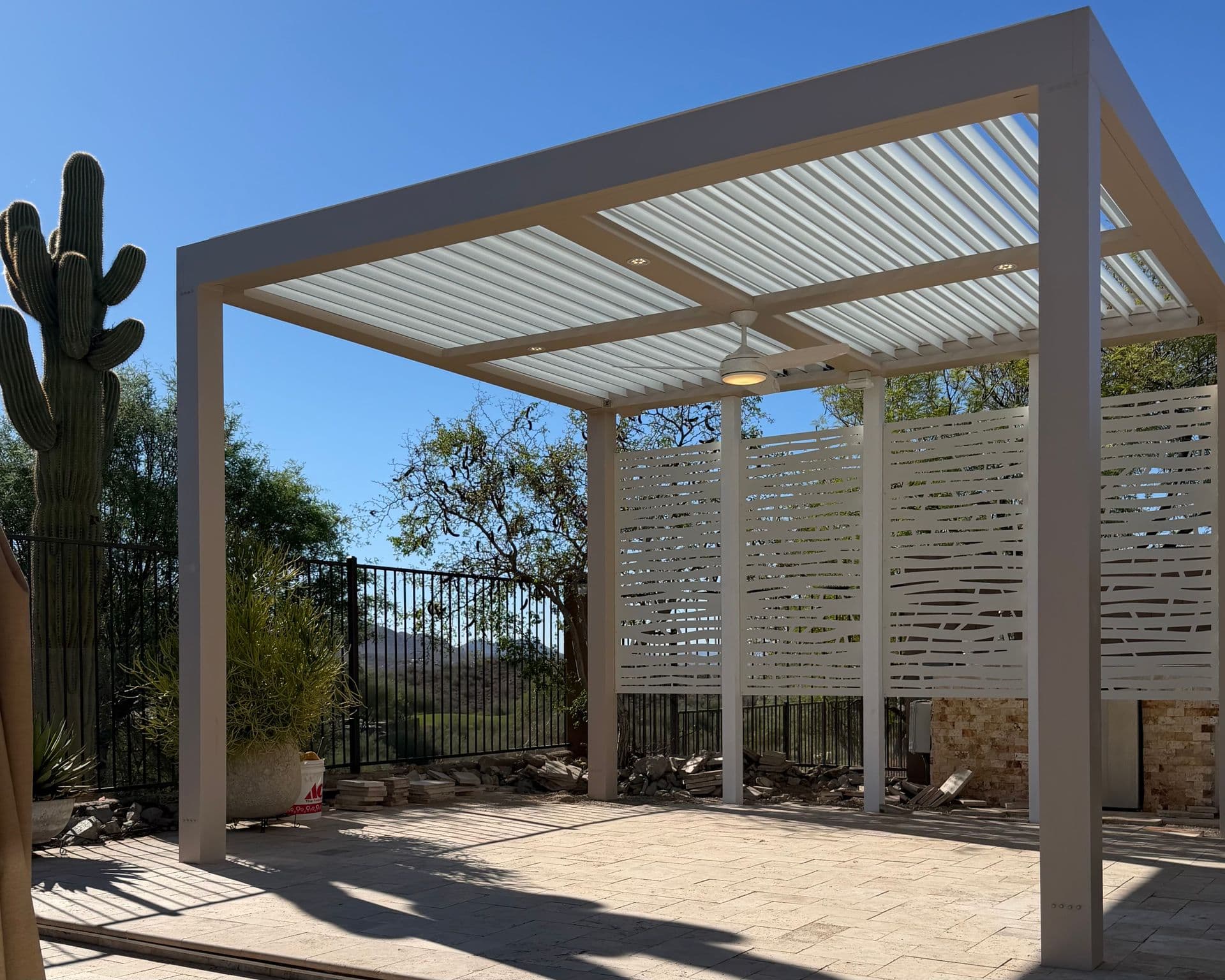 A modern aluminum pergola set in an Arizona backyard with a large cactus and desert plants.