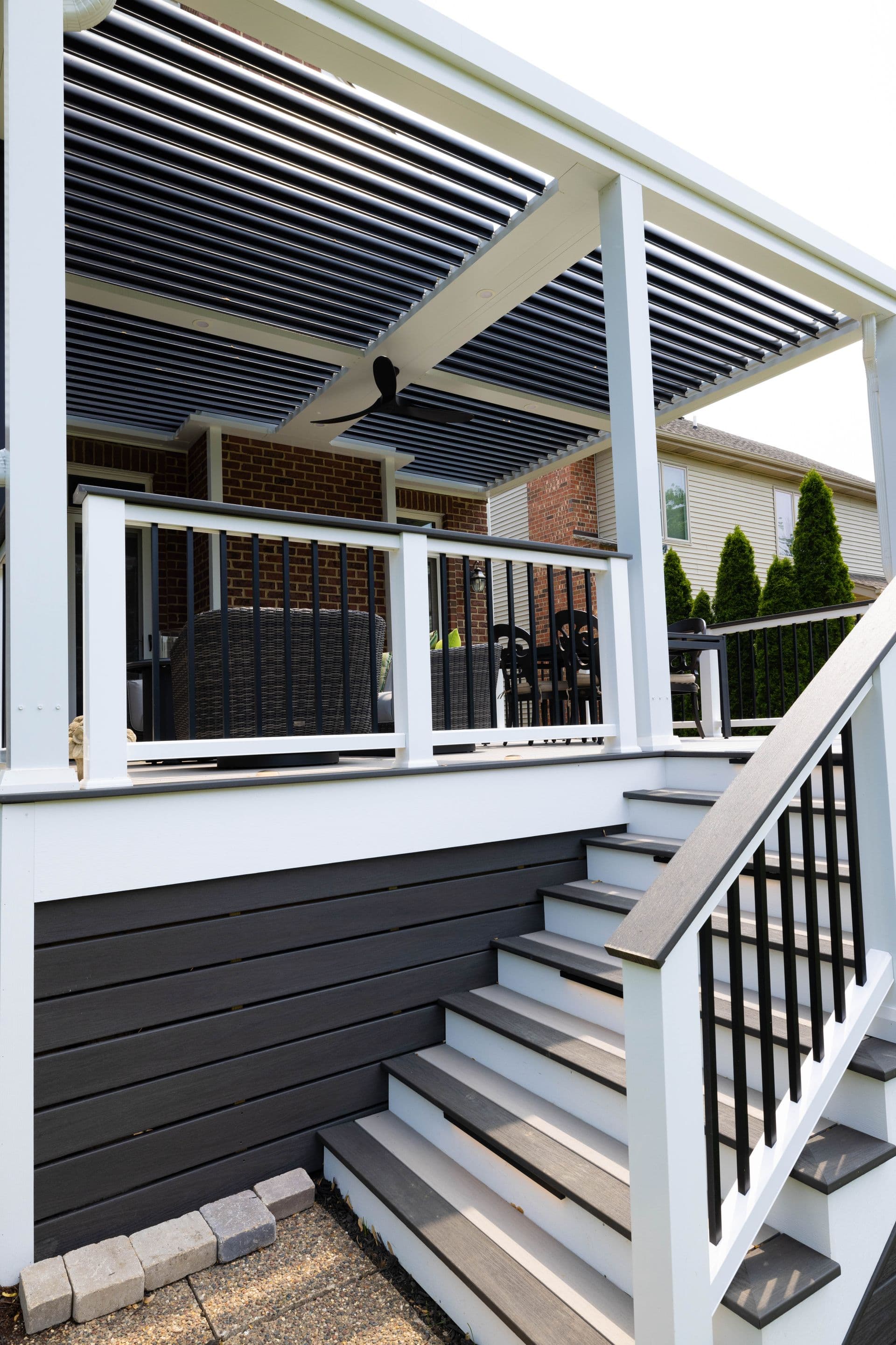 Stairs lead up to a deck covered by a white and black pergola with black hanging outdoor fans.